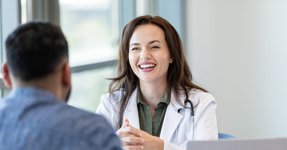 A doctor smiling and facing her patient, her laptop set to one side