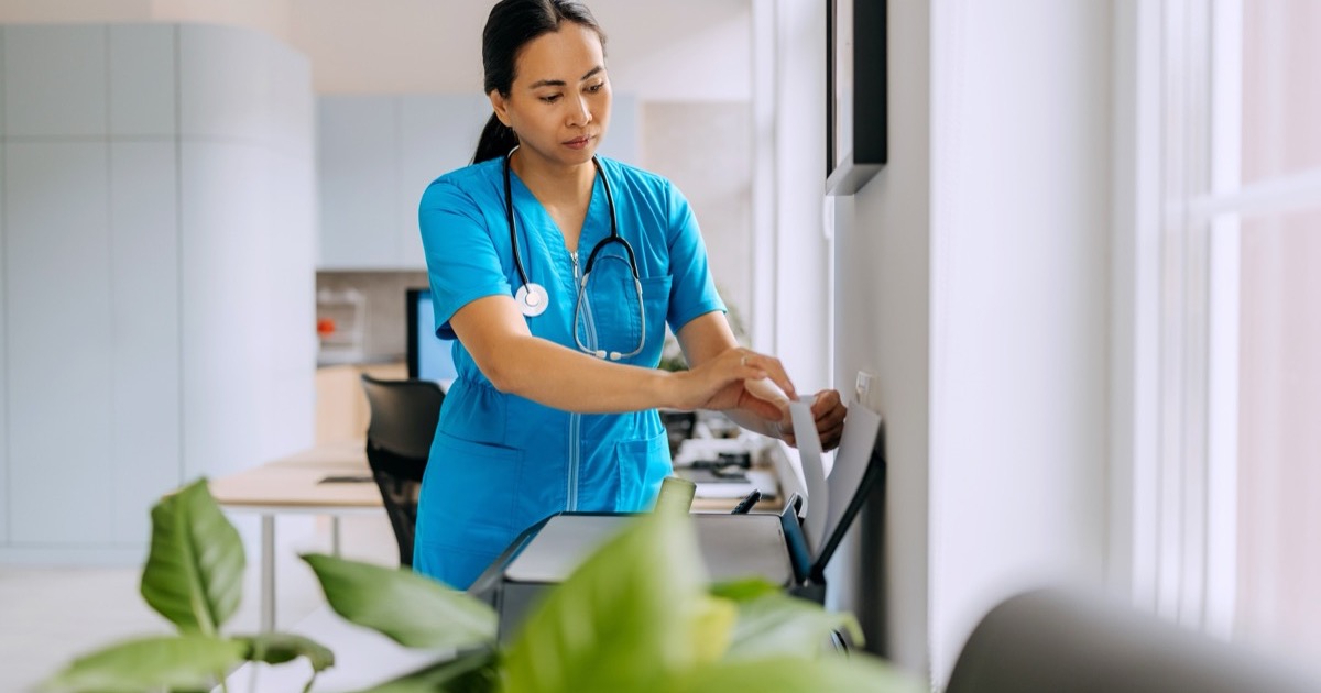 A nurse pulling pages from an office fax machine